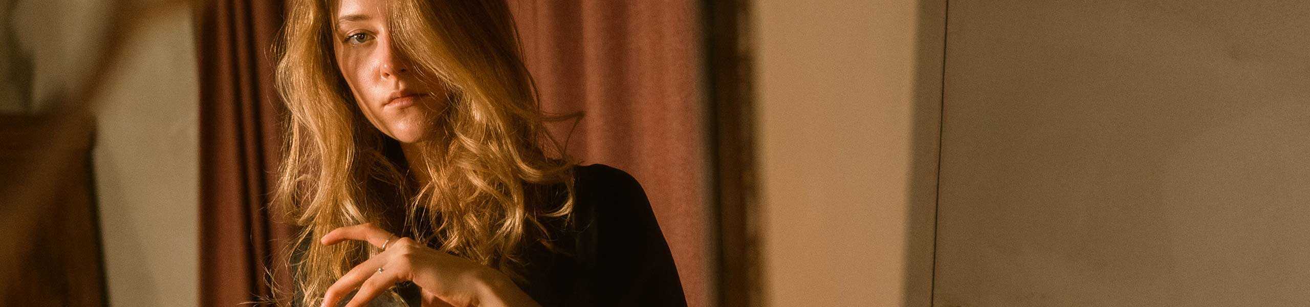 Close-up of a woman with wavy ginger hair wearing a black top, indoors at Raahni.