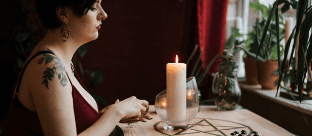 Soft-lit woman with tattooed arm meditating beside candles in cozy ambient room.