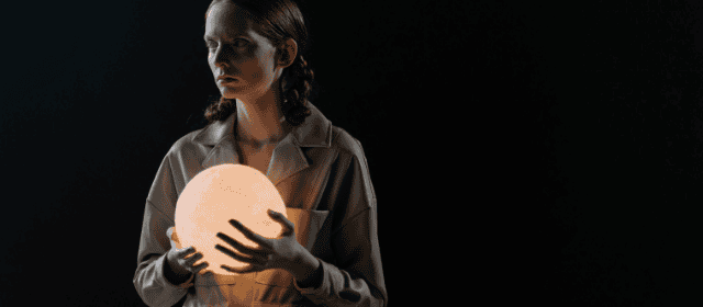 Soft glowing orb held by a woman in dark background, symbolizing illumination and mystery.